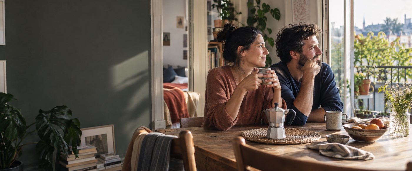 Two people sharing coffee at a sunny kitchen table, looking out of the window